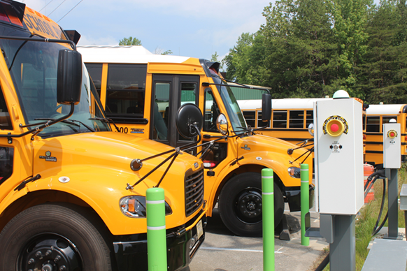 Two electric school buses are parked in from of their electric vehicle charging stations. 